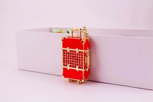 Macro shot of red rhinestone suitcase keychain with gold metal frame on a pink box