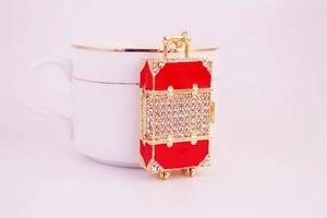 Detail of a red rhinestone suitcase keychain with gold metal frame on a white cup