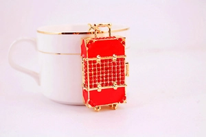 Macro shot of red rhinestone suitcase keychain with golden metal details on a white cup