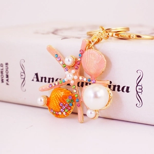 Porte-clés étoile de mer et coquillage rose avec perles et cristaux sur livre blanc