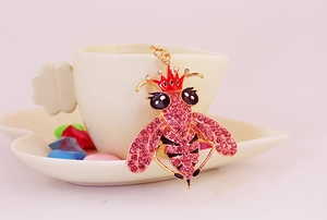 Dettaglio del ciondolo ad ape con cristalli rosa e corona rossa su tazza bianca