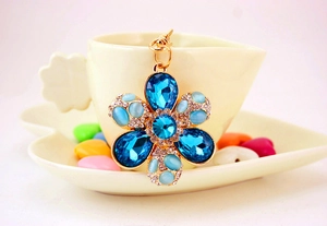Detailed view of the flower-shaped keychain with blue gems hanging on a coffee cup edge
