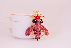 Dettaglio di un ciondolo ape in cristallo rosa con corona su una tazza bianca