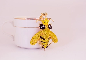 Dettaglio di un portachiavi a forma di ape regina dorata con strass appeso a una tazza