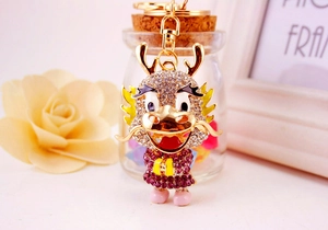 Close-up of golden dragon keychain with purple and clear rhinestones on a decorative backdrop