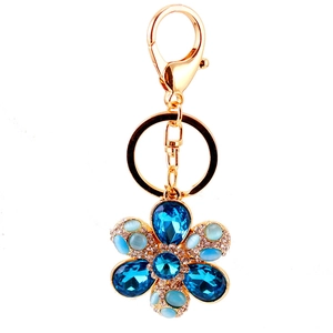 Golden flower keychain with blue crystals and opal petals on a white background
