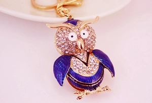 Macro view of crystal owl keychain with blue enamel inlay and polished gold-tone metal