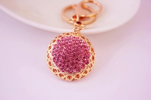 Détail du porte-clés rond en strass rose avec bordure dorée ajourée et élégante