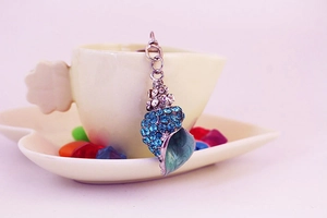 Macro detail of a colorful conch keychain featuring blue rhinestones and teal enamel finish
