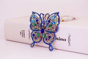 Close-up of golden butterfly keychain with blue and green rhinestones beside a book