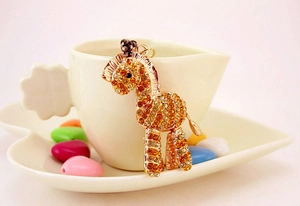 Dettaglio di un ciondolo a forma di giraffa dorata con strass color ambra e cristalli