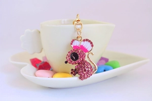 Detailed macro of a cute pink crystal mouse keychain on a white coffee cup and tray