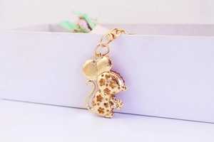 Macro detail of golden mouse keychain with red rhinestones and hollow floral pattern