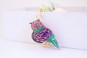 Détail d'un porte-clés oiseau avec strass violets et émail vert sur anneau doré brillant