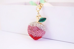 Close-up of sparkling peach keychain with pink gradient rhinestones and green leaf charm