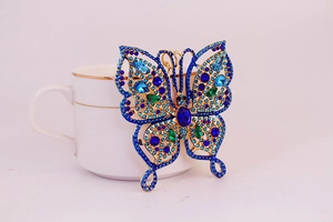 Close-up of golden butterfly keychain with blue rhinestones next to a coffee cup