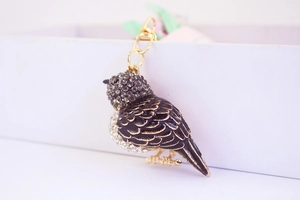 Gros plan détaillé d'un porte-clés oiseau avec strass gris et détails en émail noir