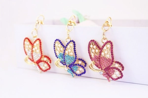 Close-up of butterfly keychains featuring colorful rhinestones and white pearls set in gold