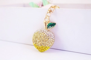 Detailed view of rhinestone peach keychain with golden lobster clasp and green enamel leaf