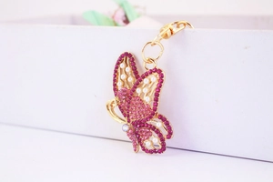 Close-up of pink rhinestone butterfly keychain with pearls and gold base on a white box