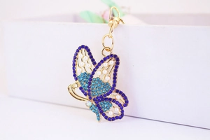 Detail of blue rhinestone butterfly keychain with pearls on a polished gold frame