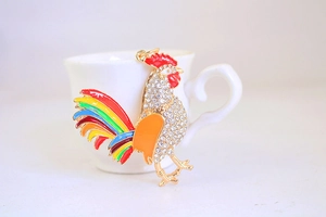 Gros plan du porte-clés coq avec plumes en émail coloré et strass brillants incrustés