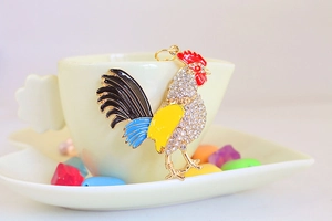 Vue détaillée du porte-clés coq en émail coloré avec strass sur une tasse en céramique