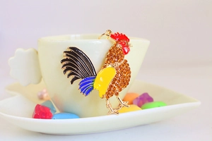 Détail d'un porte-clés coq avec cristaux ambrés et émail suspendu à une tasse en céramique
