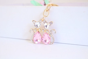 Detail of two golden cat keychains featuring pink crystal bodies and heart-shaped heads