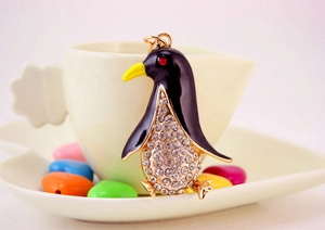 Detail of penguin pendant with white rhinestones on gold metal hanging on a white coffee cup