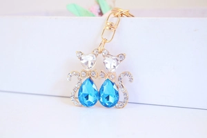 Close-up of golden dual-cat keychain with blue teardrop crystals and sparkling rhinestones