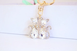 Macro shot of twin cat keychains featuring heart-shaped crystals and gold alloy base