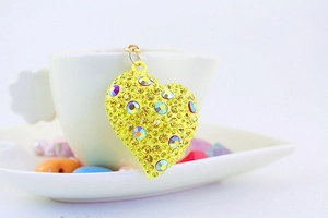 Dettaglio di un portachiavi a cuore con strass gialli appeso al bordo di una tazza bianca