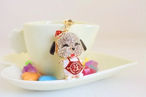 Detail of a gold puppy keychain with rhinestones and a red bib featuring the Cai symbol