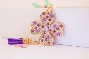 Détail d'un porte-clés trèfle doré avec des strass violets et un gland en daim doux