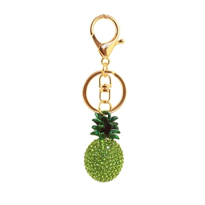 Close-up of a sparkling gold pineapple keychain with green rhinestones on white background