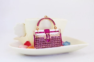 Glitzernder Strass-Handtaschen-Anhänger in Magenta-Emaille auf weißer Untertasse