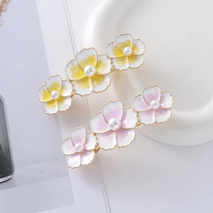 Dettaglio di fermagli per capelli con fiori gialli e rosa e perle su piatto bianco