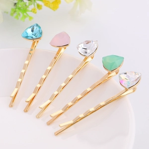 Detail view of five wavy gold bobby pins set with colorful geometric crystals on white ceramic