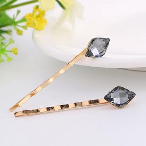 Close-up of golden hair clips featuring faceted gray crystals on a white surface