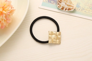Close-up of a black elastic hair tie featuring a golden square alloy buckle with woven texture