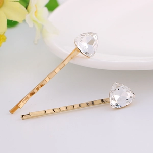 Close-up of golden alloy hair clips with heart-shaped crystal and wavy metal texture