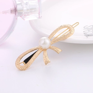 Elegant gold bow hair clip with brushed texture and large pearl on a white plate