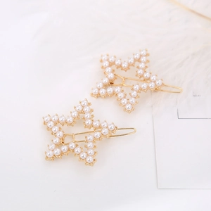 Close-up of elegant star-shaped gold hair clips with white pearls on a minimalist background