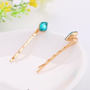 Detail shot of golden alloy hair clips with vibrant blue square crystal on a white plate