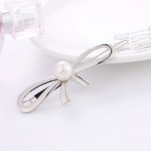 Elegant silver metal bow hairpin with central pearl detail on a white ceramic plate