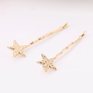 Detail of two star-shaped gold hair clips with hammered matte texture and wavy pins
