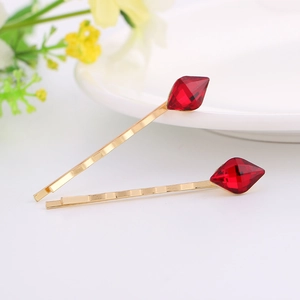 Elegant gold metal hair clips with red crystals and wavy texture on white ceramic plate