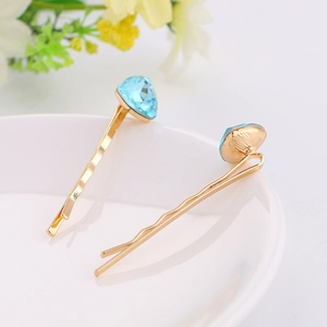 Close-up of golden wavy hairpins with light blue crystal heart on white plate