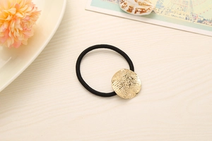 Detail of high-elastic black hair tie featuring a textured golden round alloy charm